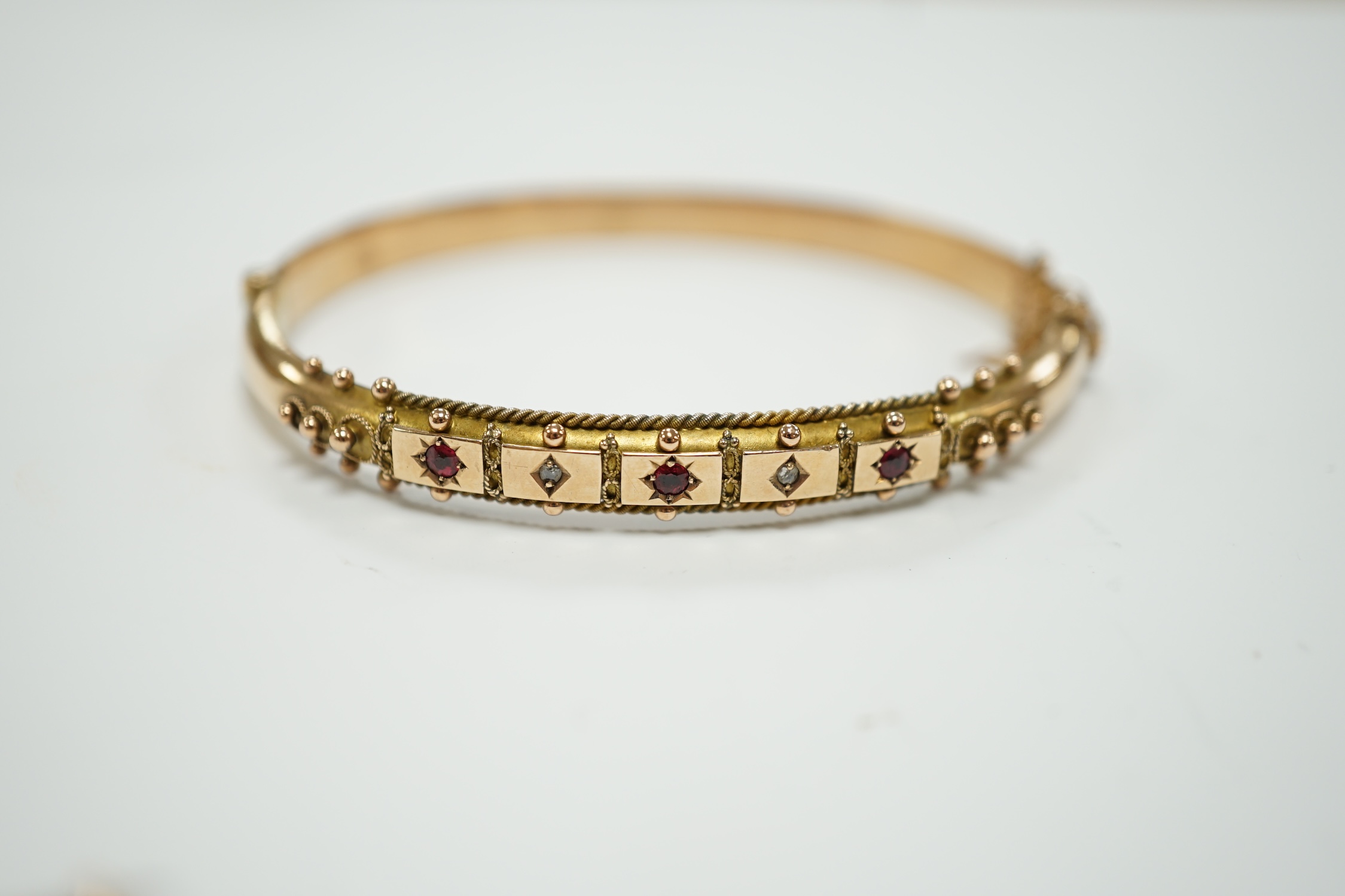 An Edwardian 9ct gold ruby and diamond chip set hinged bangle and a similar yellow metal, ruby and diamond chip set bar brooch, gross weight 12.1 grams.